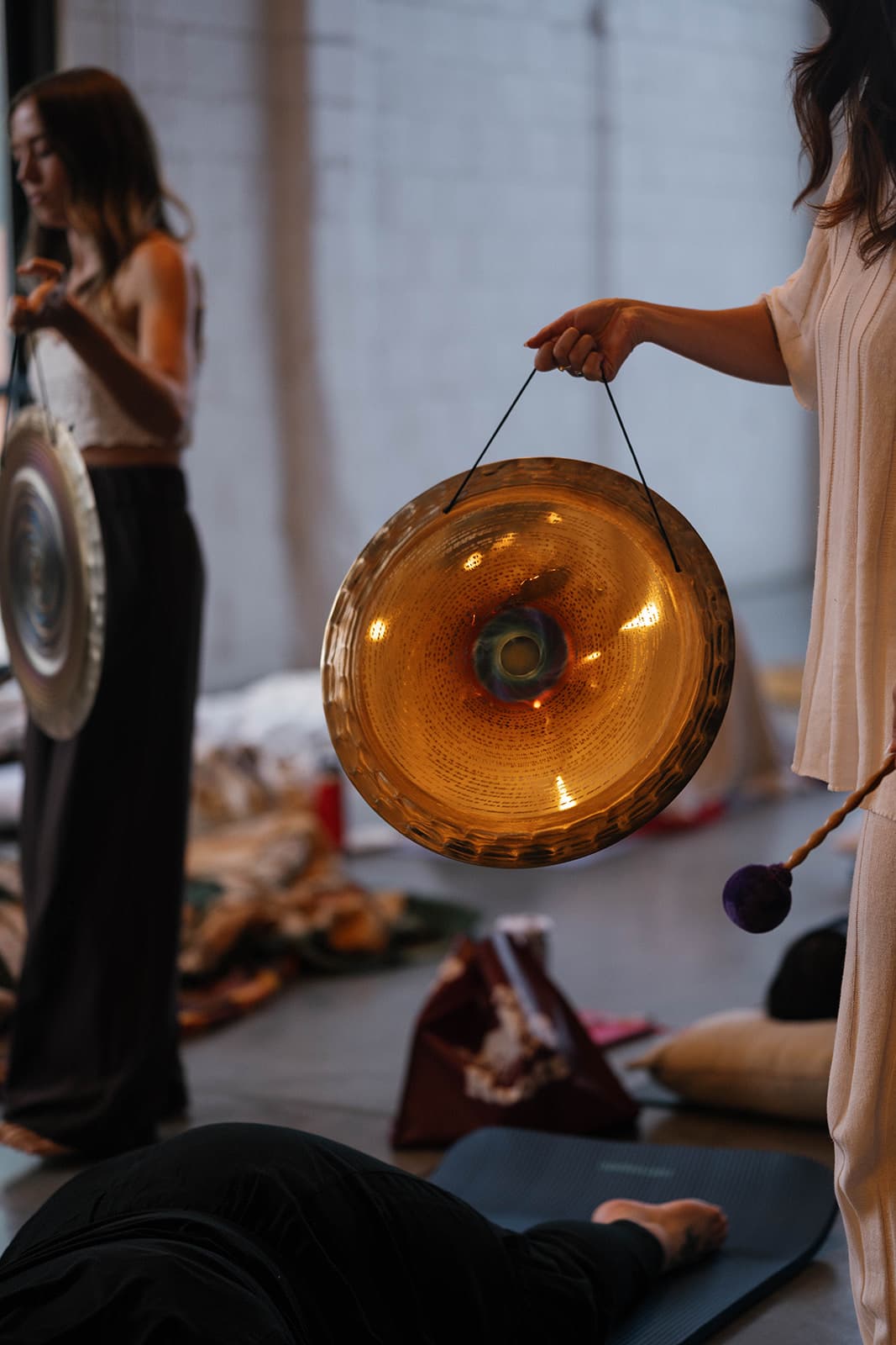 A glowing gong held up during a group sound bath while guests rest on mats