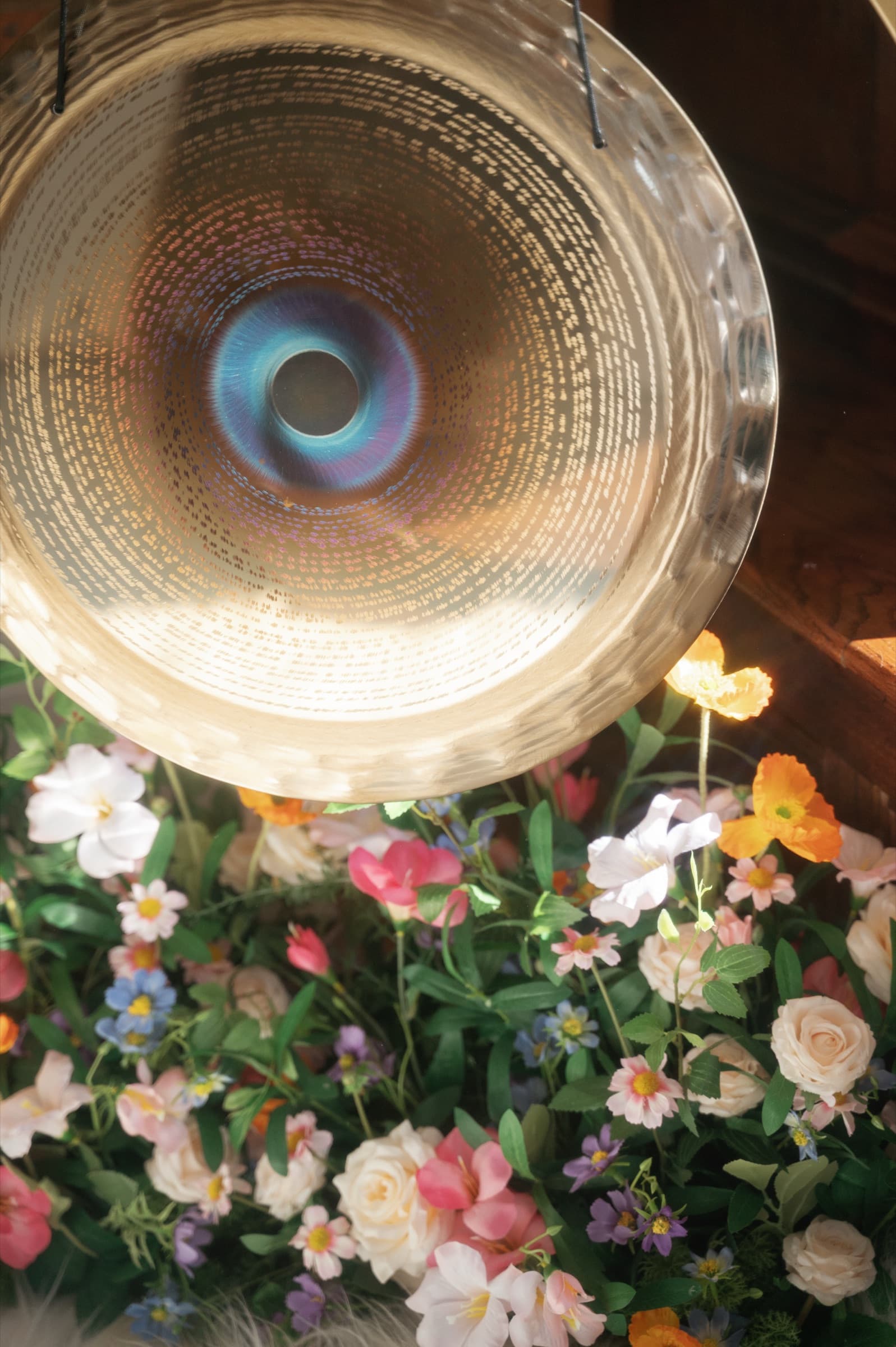 An iridescent gong above a bank of roses, ranunculus, and wildflowers in Laura's studio