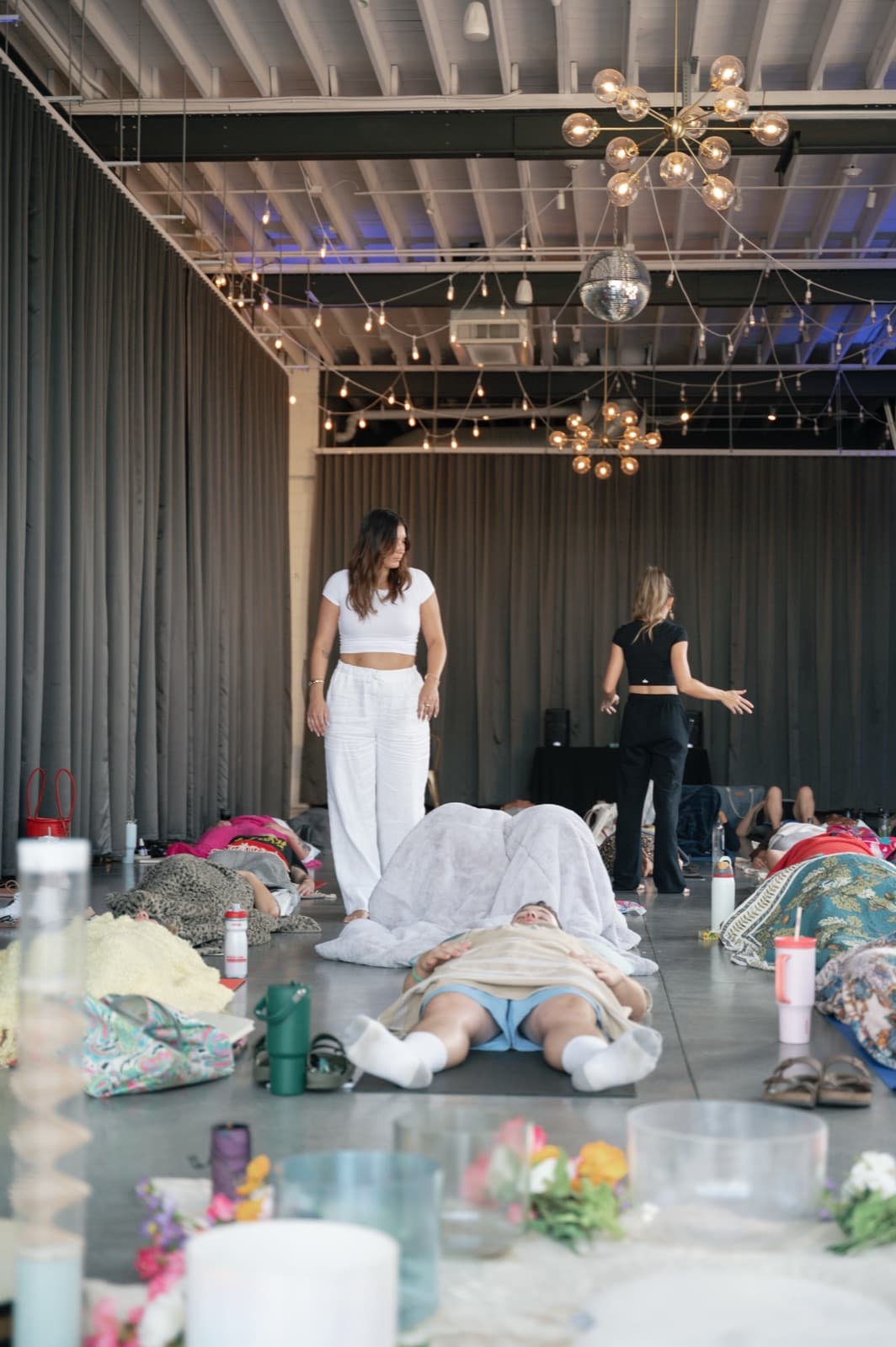 Guests lying on mats under string lights while Laura and a co-facilitator guide a group sound bath
