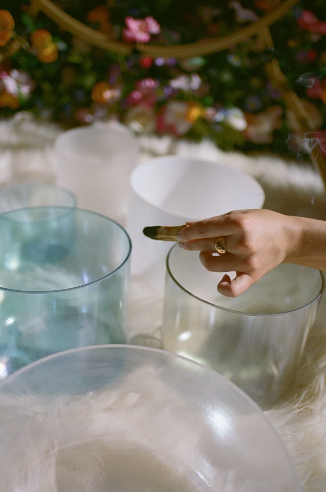Laura seated among crystal singing bowls and gongs, eyes closed, beside a bank of flowers