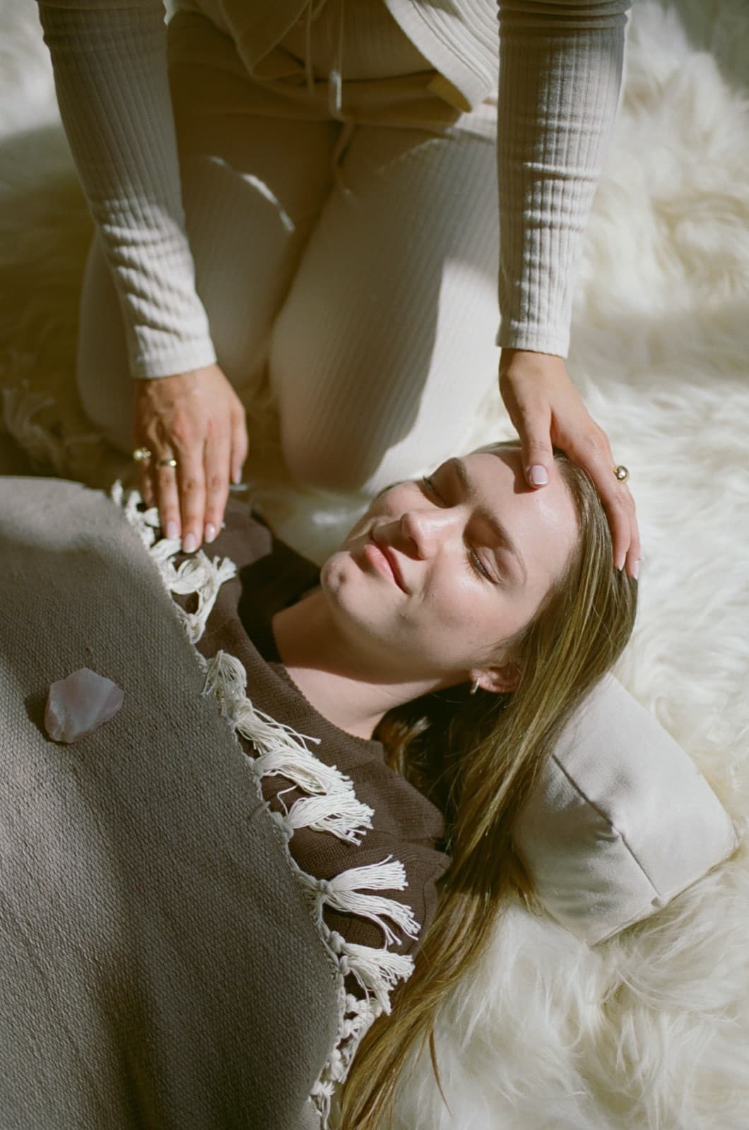 Laura resting her hands on a client's head as she lies on sheepskin in soft window light